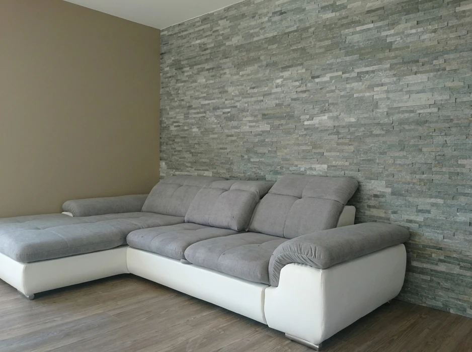 Deux hommes installent du papier peint à motifs ornementaux beige dans un intérieur résidentiel avec moulures blanches
